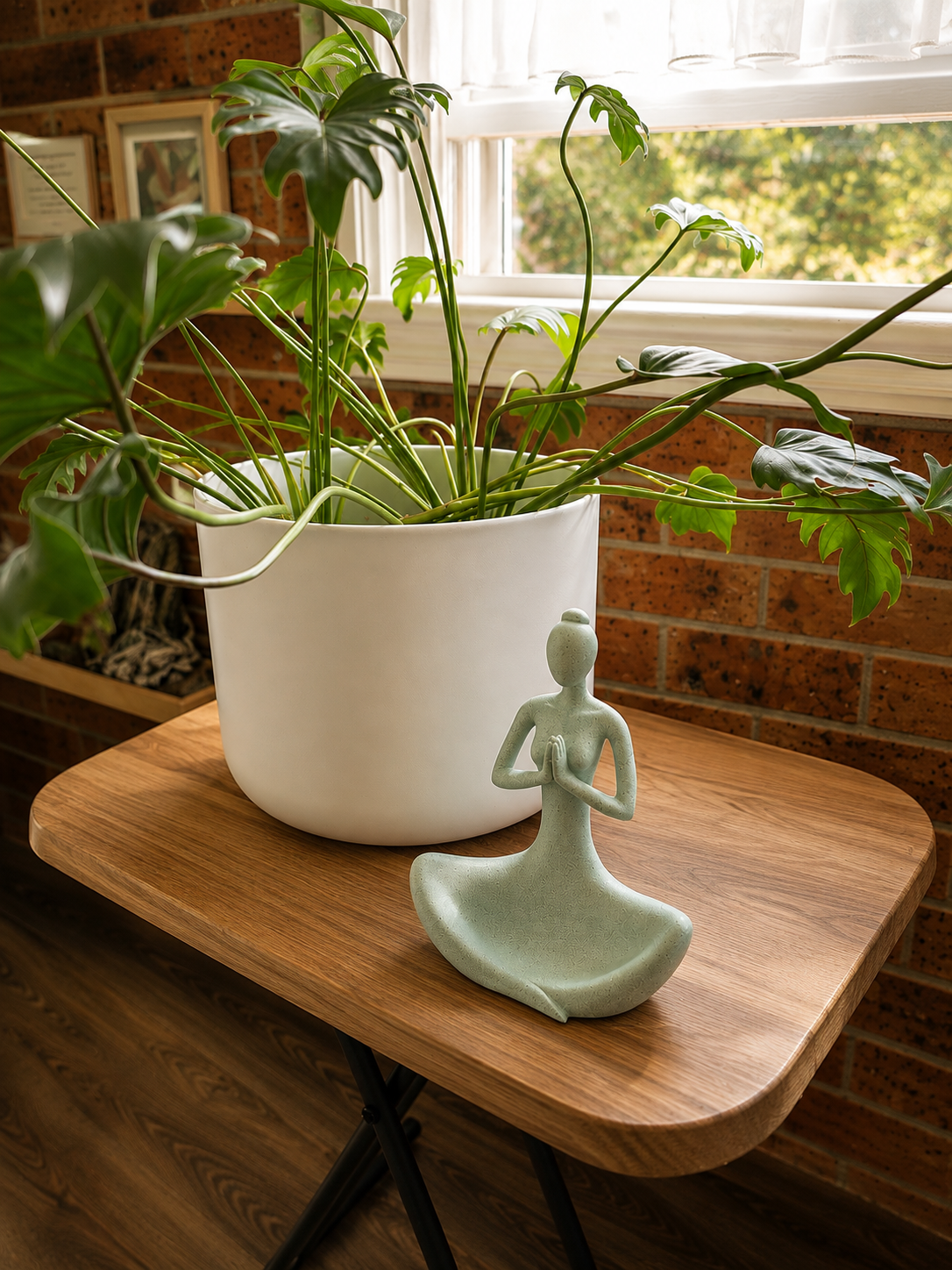 A leafy indoor plant beside a small meditating figurine on a wooden table